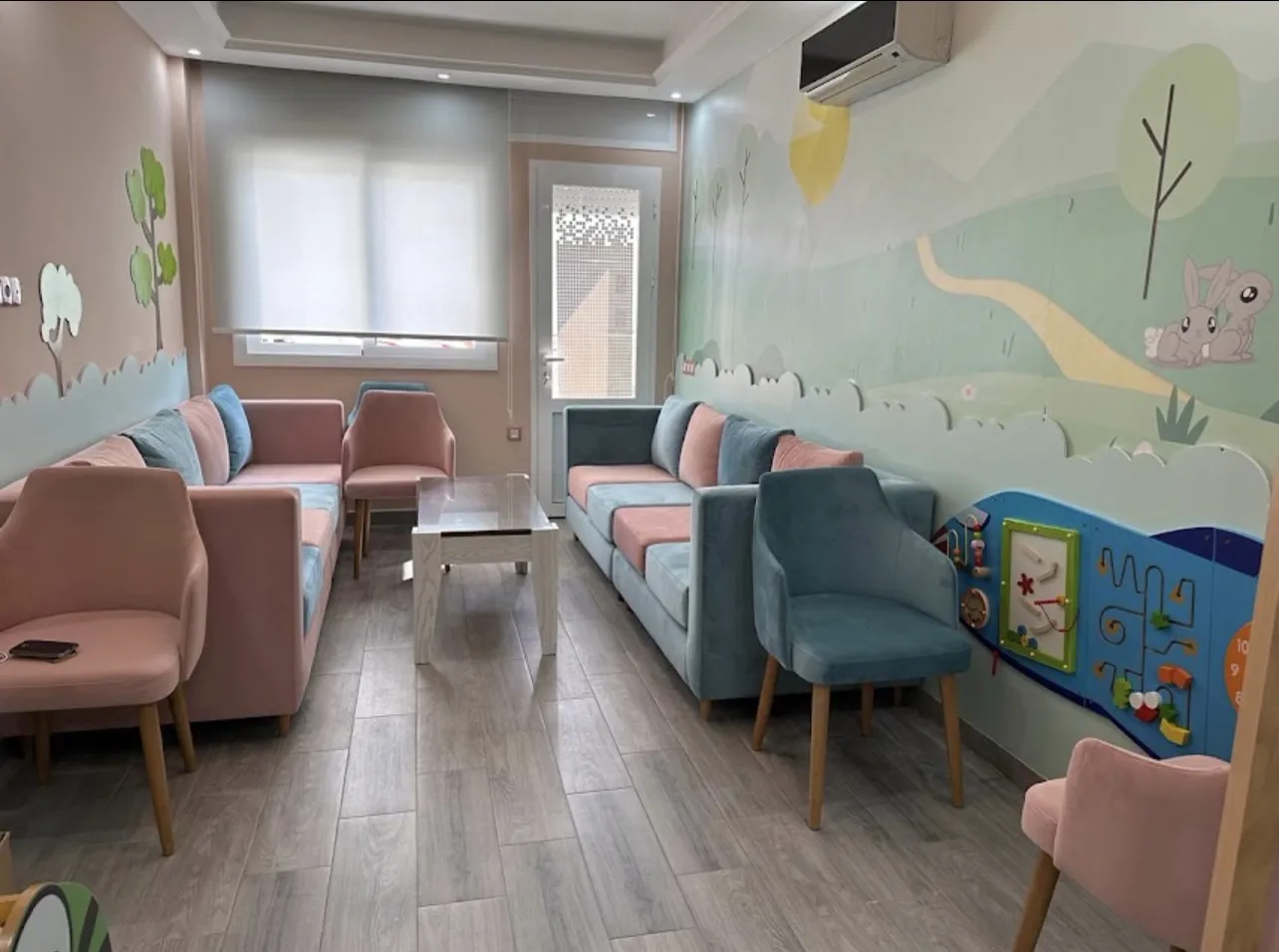 Salle d'attente aux canapés rose et bleu, avec une fresque de forêt et de lapins