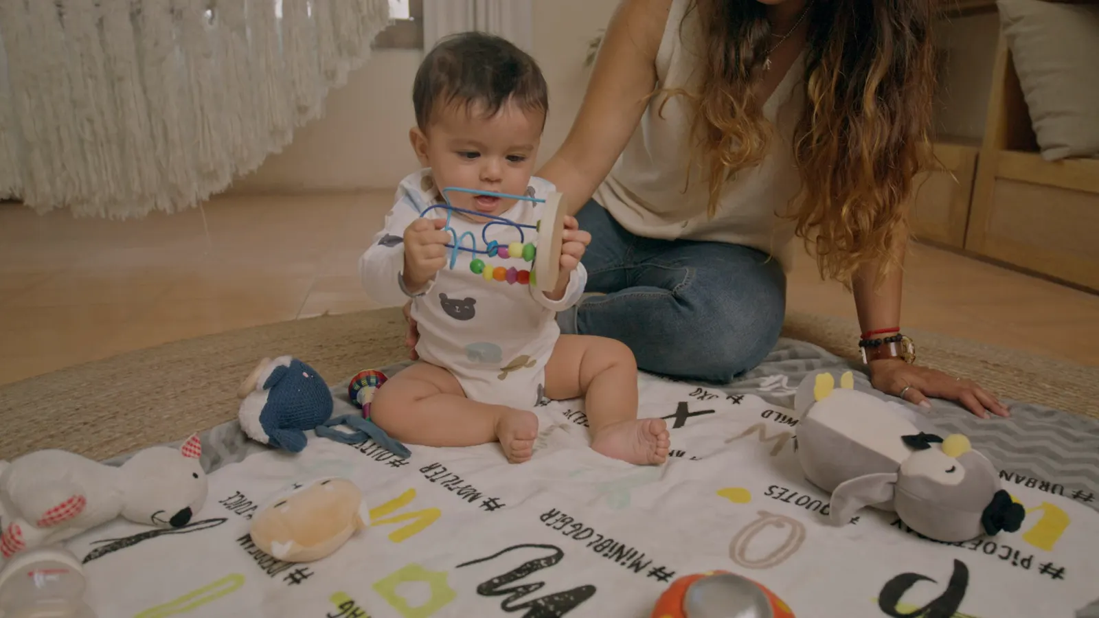 Une maman joue avec son bébé assis sur un tapis d'éveil